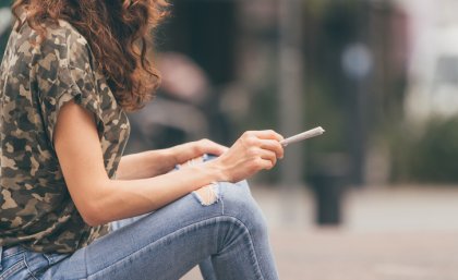 Image of a woman wearing jeans sitting down with a joint in her hands 